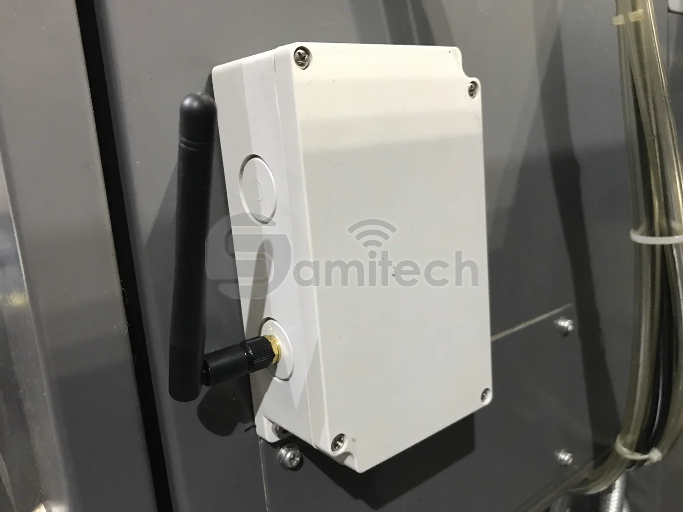 Hộp nhựa trắng kín gắn trên vỏ máy màu xám, ăng-ten đen đưa ra ngoài qua đầu nối ở cạnh hộp.